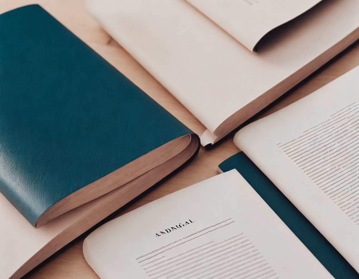 Teal Hardcover Book on Wooden Surface Amid Open Text-Filled Books