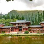 Serene pond reflects red Japanese buildings surrounded by cherry blossoms