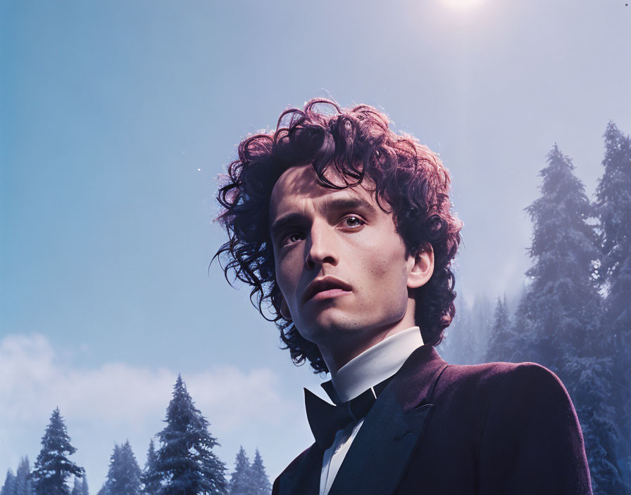 Young man in tuxedo with curly hair in misty forest setting