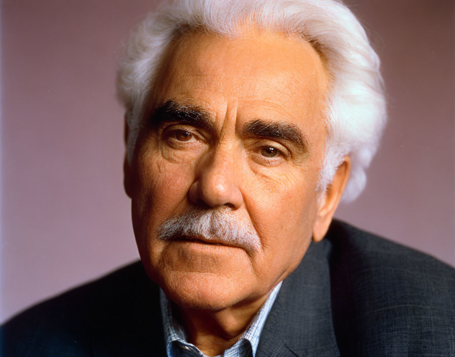 Elderly man with white hair and stern expression on pink background