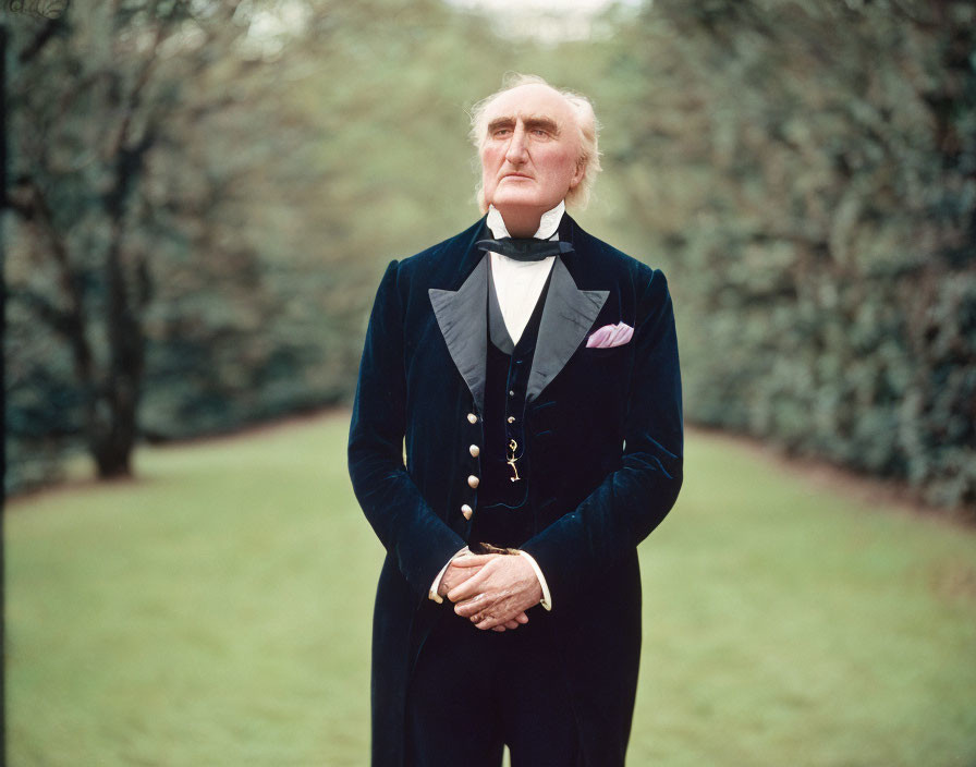 Elderly gentleman in vintage blue tailcoat and white tie against green trees