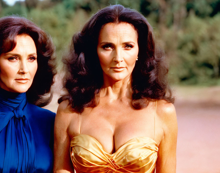 Two women in blue and gold outfits with dark voluminous hair