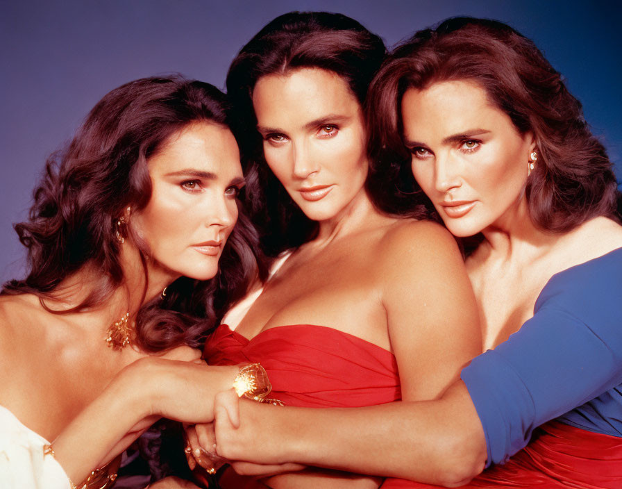 Three women posing in elegant red and blue attire against blue backdrop