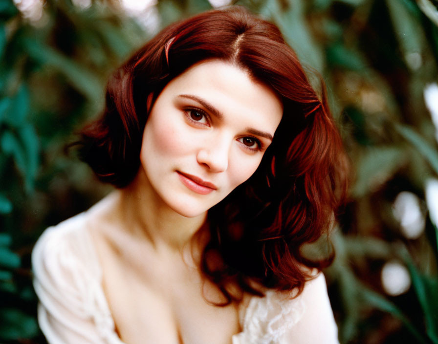 Portrait of woman with shoulder-length brown hair and white top against green foliage