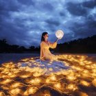 Woman in yellow gown surrounded by sunflowers under large blue bird in moonlit sky