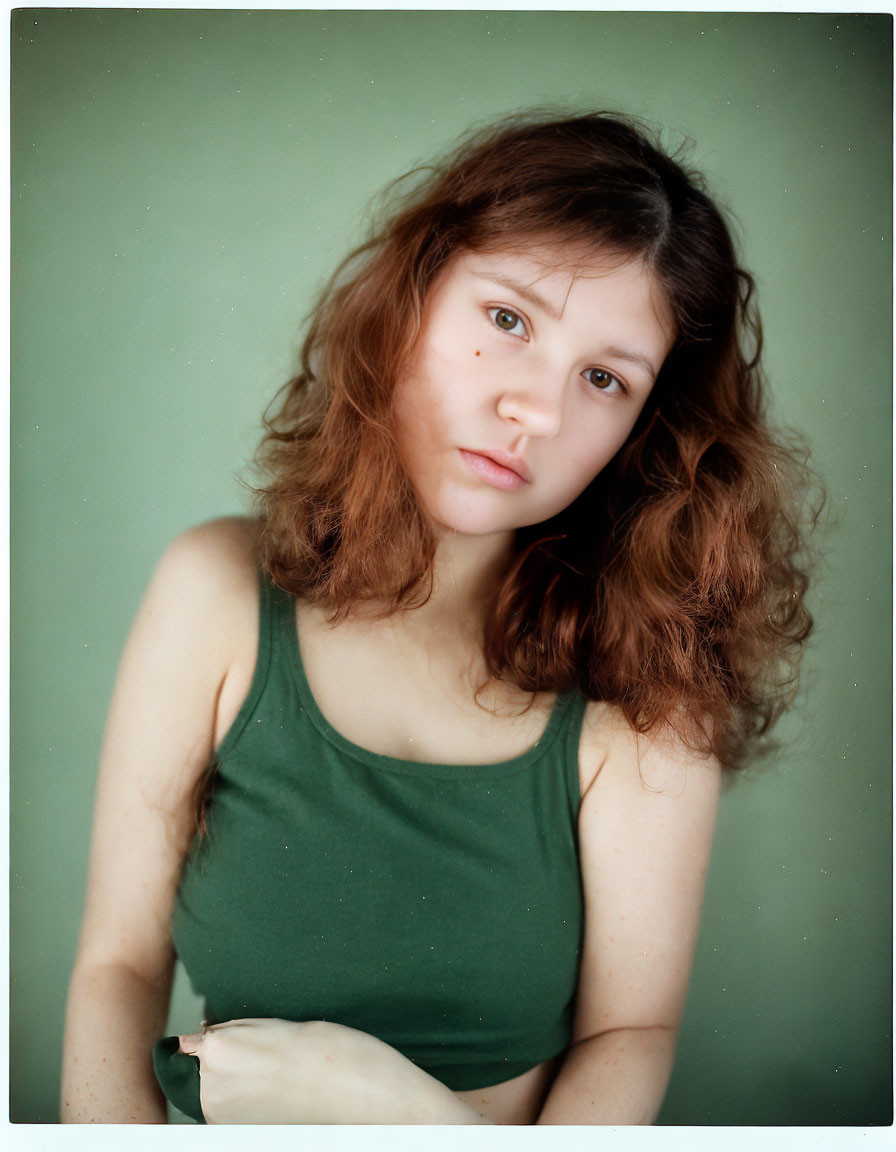 Young Woman with Curly Hair in Green Tank Top Against Greenish Backdrop