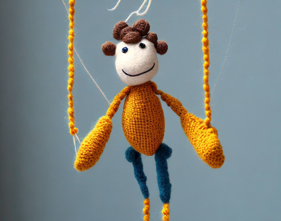 Handmade knitted giraffe toy on strings against soft blue background