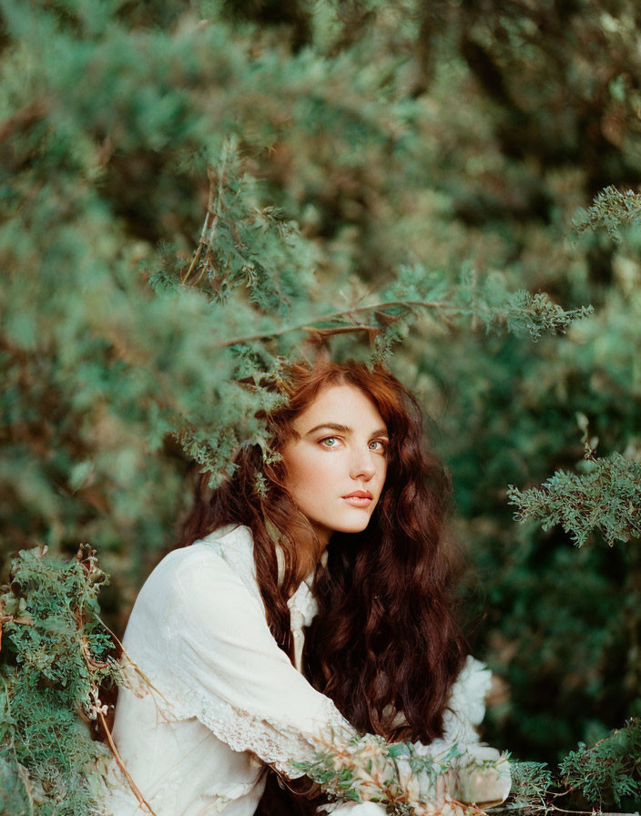 Woman with long dark hair in white blouse amidst lush greenery