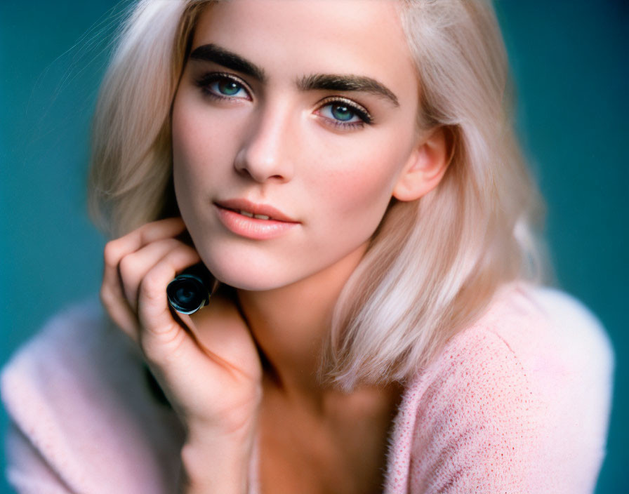 Portrait of woman with platinum blonde hair, prominent eyebrows, fair skin, in pink top.