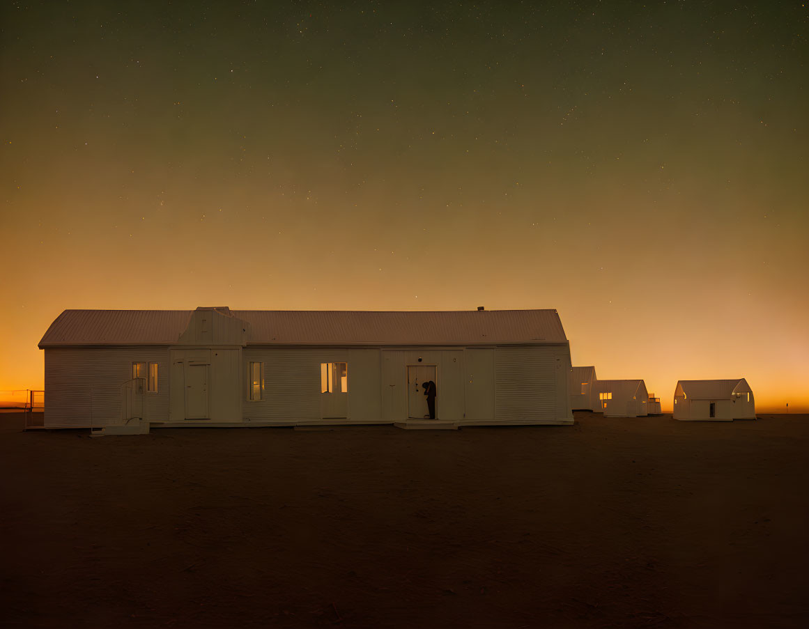 Nighttime scene: Isolated buildings under starlit sky and orange horizon.