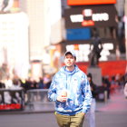 Young person in blue hoodie and khaki pants walking with coffee cup on sunny urban street