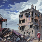 Solitary figure in red coat views demolished building with excavator among rubble