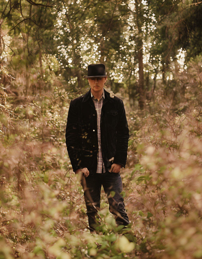 Man in Black Jacket and Hat Standing in Sunlit Forest