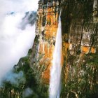 Majestic waterfall on sheer cliff with golden sunlight and mist