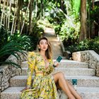 Woman in Golden Floral Dress Amidst Blossoming Pathway Under Tree Canopy