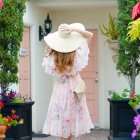 Woman in white dress with wide-brimmed hat by floral door