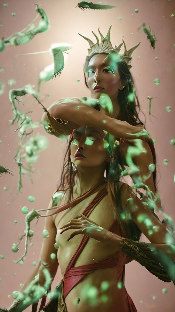 Two women in ethereal attire with crown, surrounded by green particles on pink backdrop