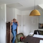 Man in denim jacket and hat photographing rustic room with person at table