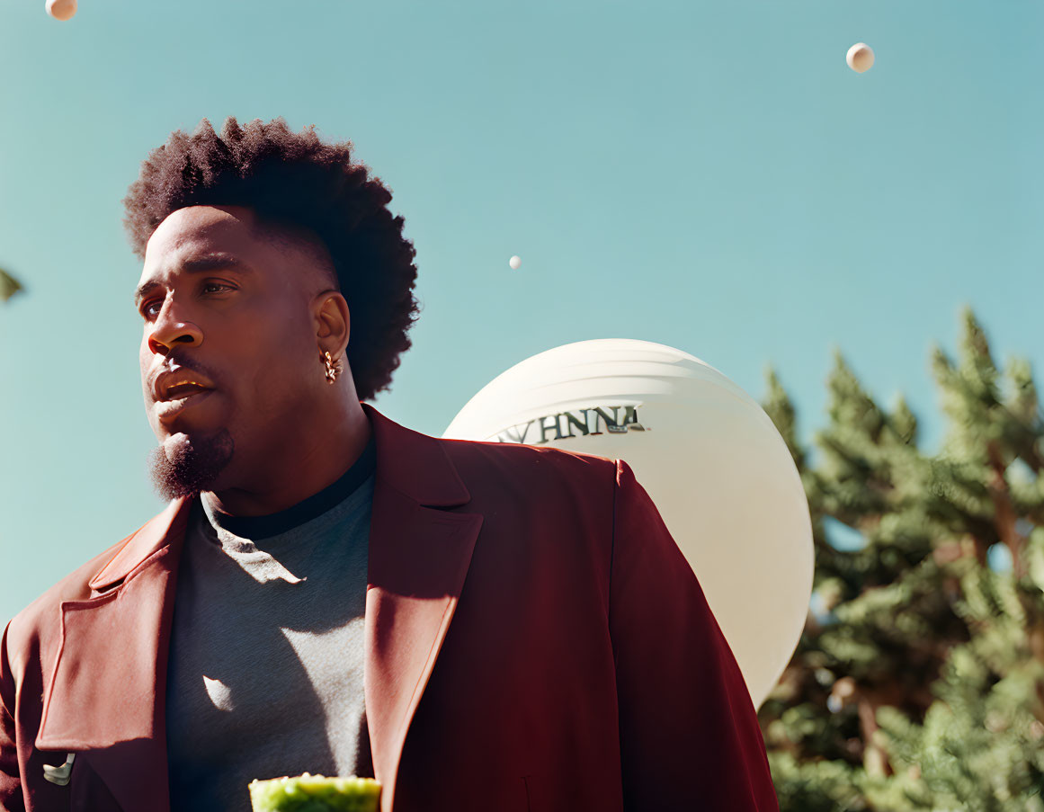 Stylish man in burgundy jacket outdoors with blue sky and white balloon.