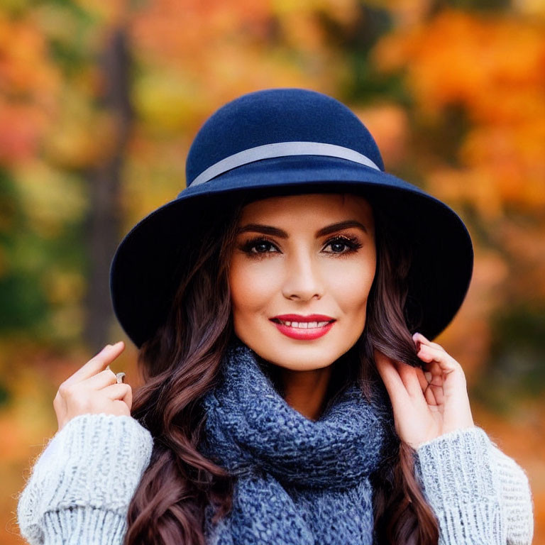 Long-haired woman in blue hat and gray scarf against autumn leaves backdrop.