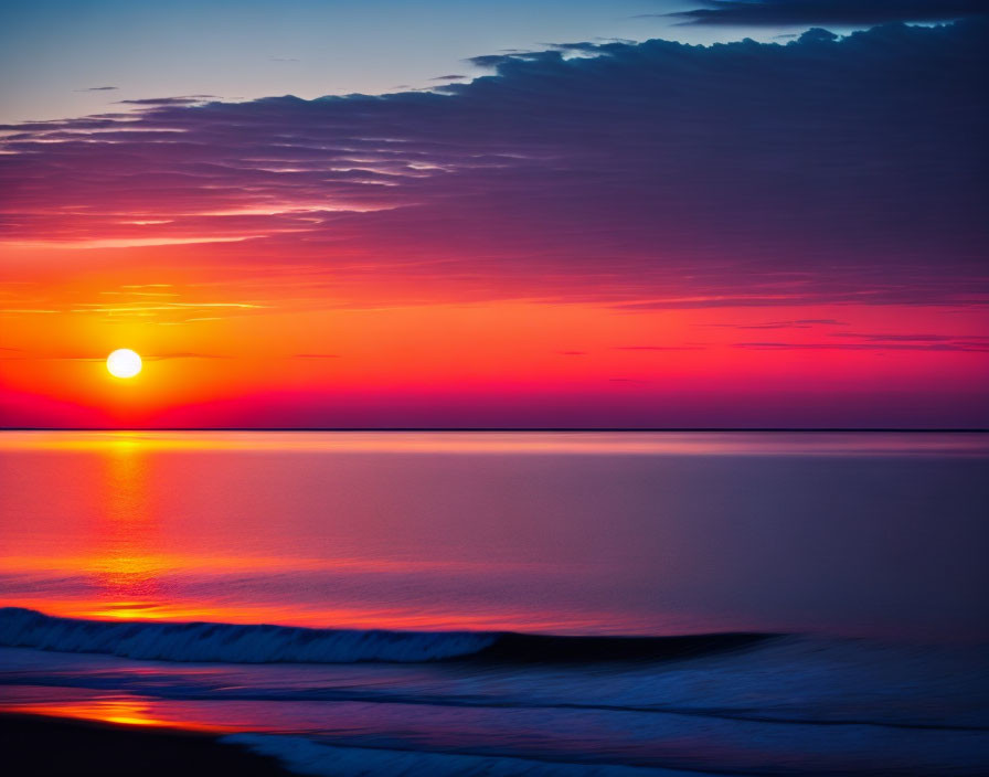 Colorful sunrise over ocean with red and purple hues reflecting on water.