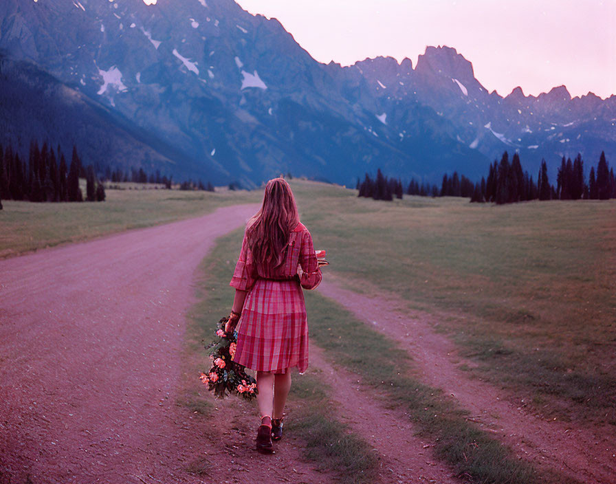 Plaid dress woman walking on dirt road with mountain backdrop