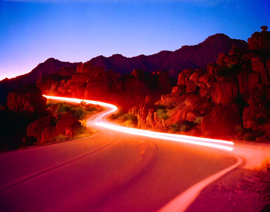 Twilight sky over rocky terrain with winding road and light streaks