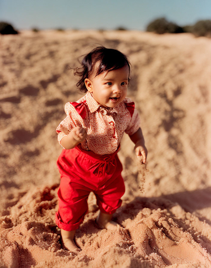 Smiling toddler in red outfit on sandy beach