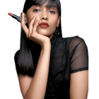 Dark-haired woman applying red lipstick on black background