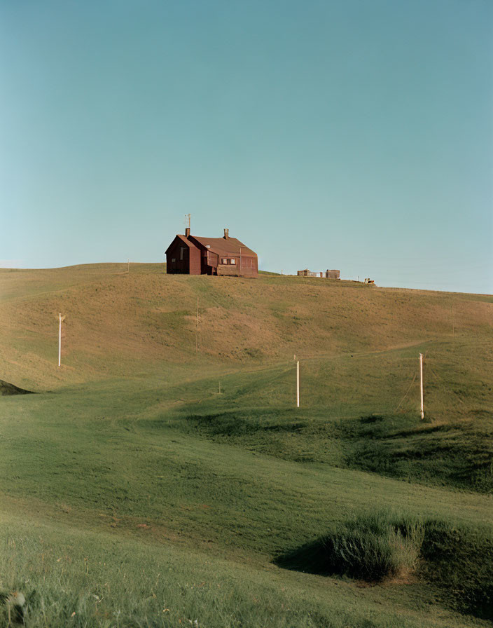 Scenic landscape with green hills, house, and utility poles under blue sky