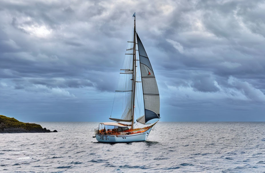 Sailboat with white sails on open sea under dramatic sky