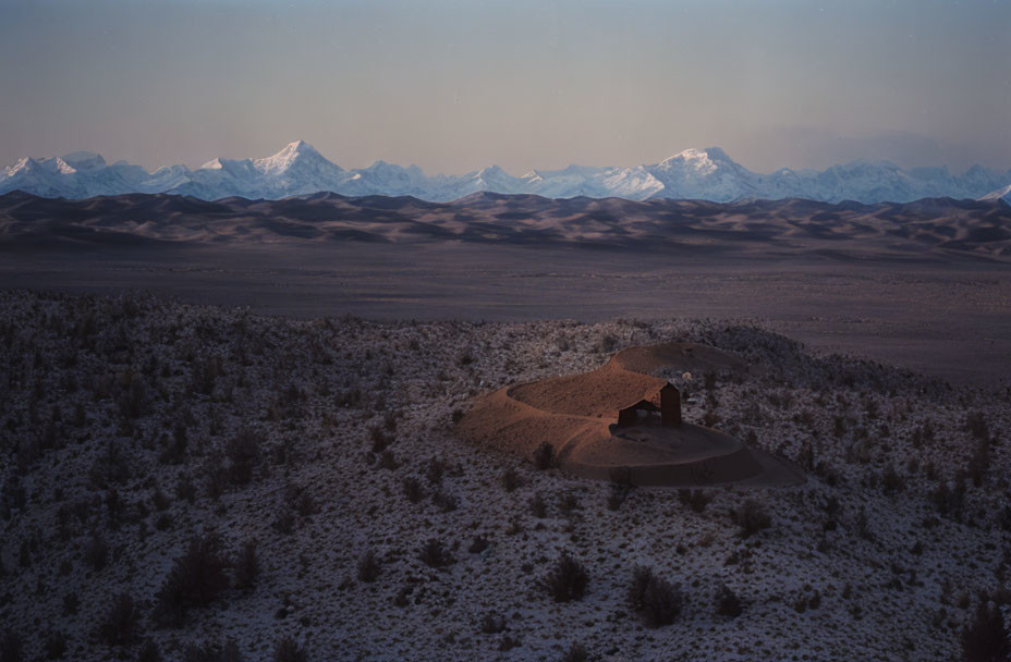 Solitary structure in snowy desert with mountains at dawn