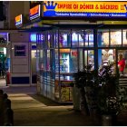 Bustling corner restaurant at night with warm lighting and patrons dining.