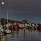 Harbor scene at dusk: boats, red & white houses, full moon