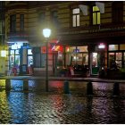 Vintage lamps, wet cobblestones, colorful umbrellas in charming evening street scene