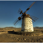 White windmill with four blades on stone base against cloudy blue sky and golden field