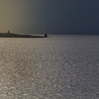 Lighthouse on rocky outcrop with stormy clouds and shimmering sunlight