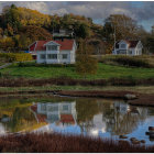 Tranquil rustic landscape with houses reflected in pond amid lush greenery