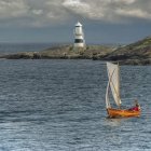 Sailboats near lighthouse on calm sea with rocky outcrops