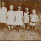 Seven Identical Girls in Vintage Dresses Pose in Blooming Garden