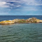 Rocky, sandy islands in vibrant blue sea under cloudy sky