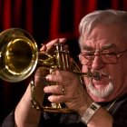 Elderly man in military uniform playing trumpet on dark backdrop