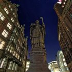 Robed figure statue in cobblestone alley at night