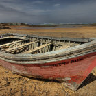 Weathered boat on sandy ground under dramatic sky with distant wind turbines