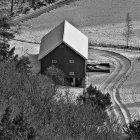 Red barn in snow-covered forest with autumn leaves peeking.