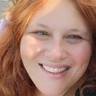 Curly Red-Haired Woman Smiling in Dappled Sunlight