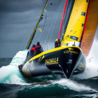 Black and yellow sailboat racing through rough seas with crew battling strong winds