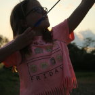 Young person at sunset in tie-dye shirt pretends to shoot arrow with stick and string.