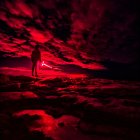 Solitary figure under crimson sky with glowing hand beam