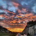 Vivid sunset painting with orange and blue sky, figures walking on illuminated path.